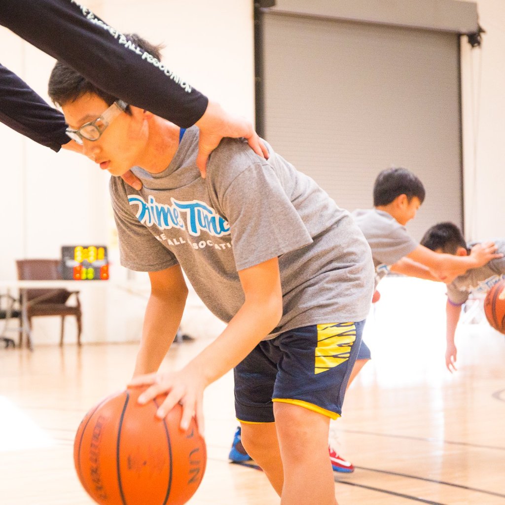 Basketball camper works on dribbling with coach during winter break basketball camp